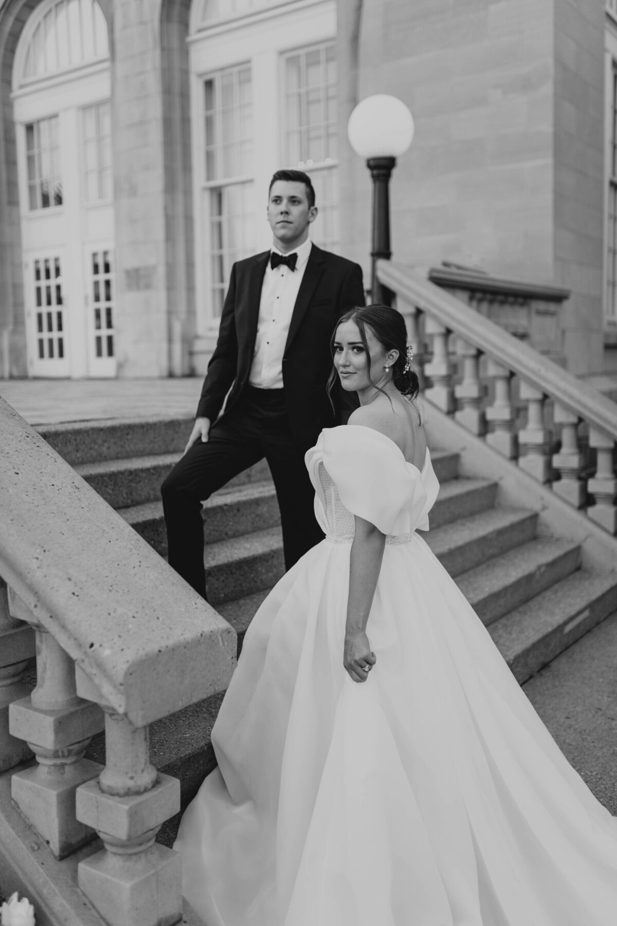 Black and white photo of a bride and groom posing on stairway.