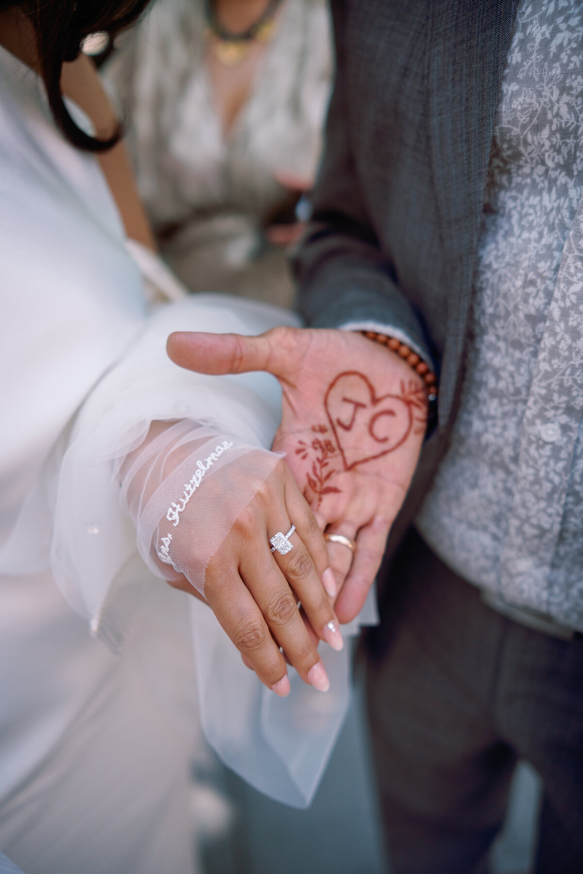 Close-up of the bride’s engagement ring resting on the groom’s hand decorated with a henna heart reading “J + C,” photographed outside New York City Hall during Japna and Chris’s elopement by NYC wedding photographer Perry Hancock.