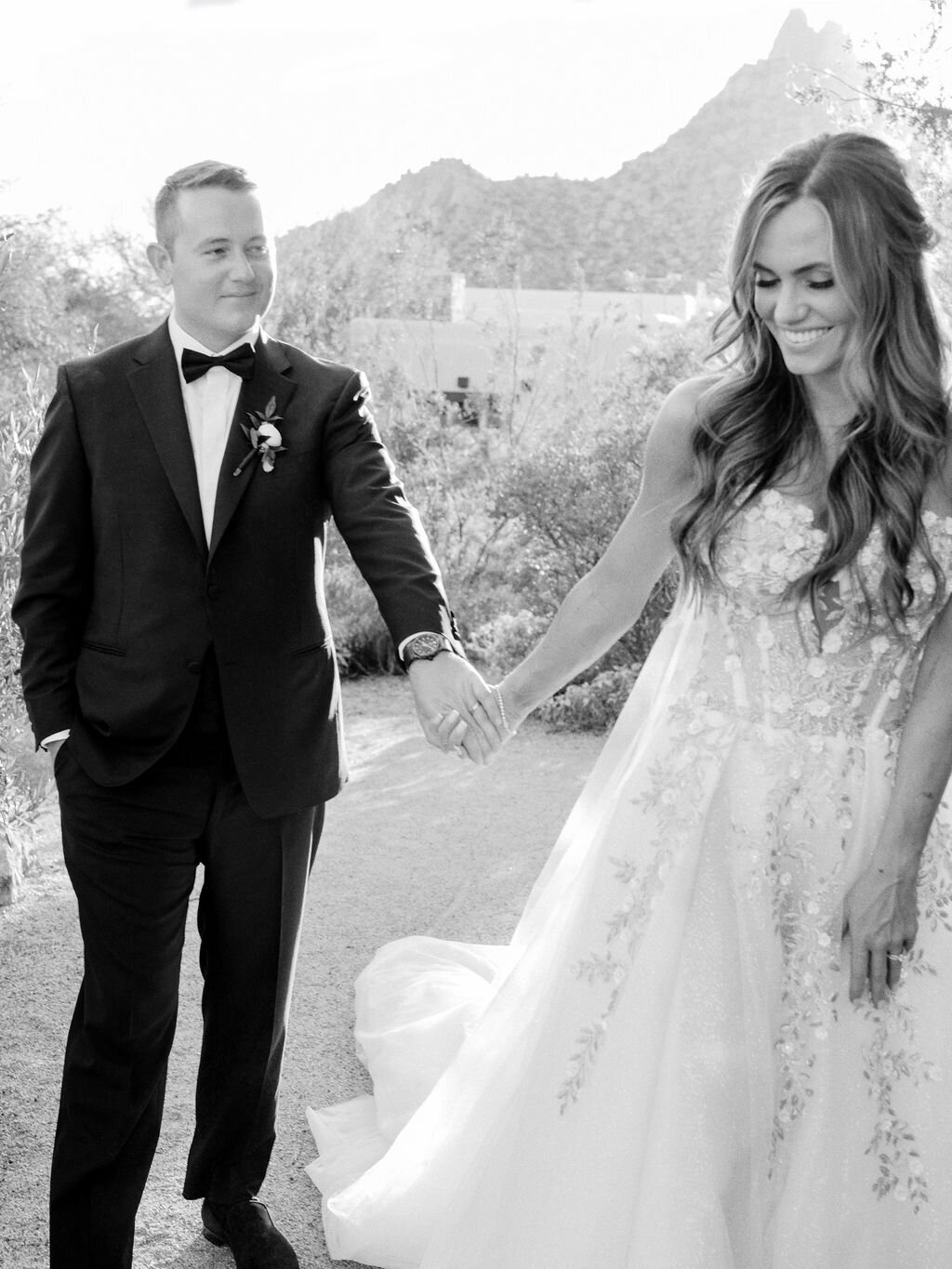 A stunning bride and groom walking hand-in-hand in the scenic desert landscape of Scottsdale. Capturing the magic of a luxury outdoor wedding.