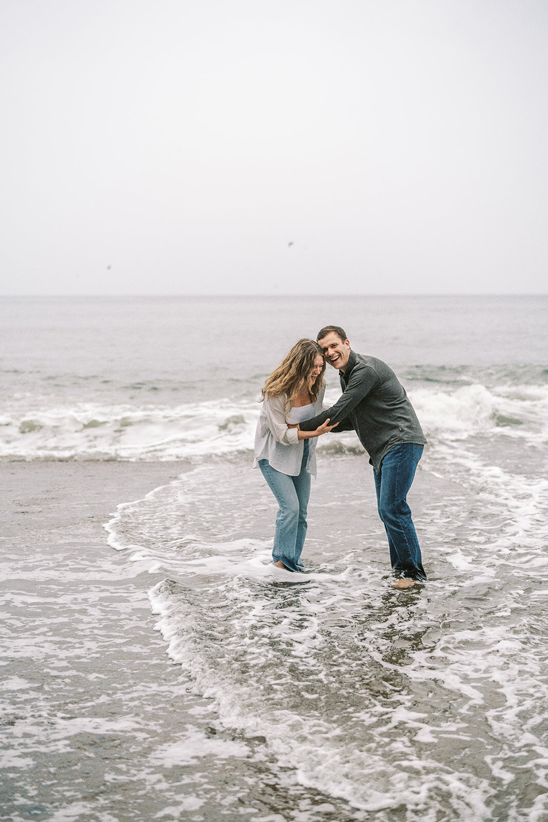 A couple laughing in the waves at the beach. 