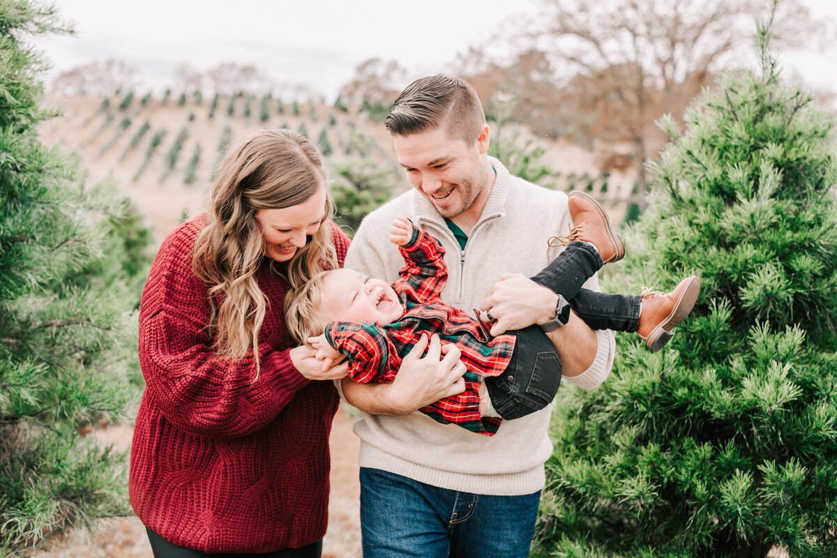 Parents smile at their little toddler as they tickle laughs out of him during their Birmingham Family Session.