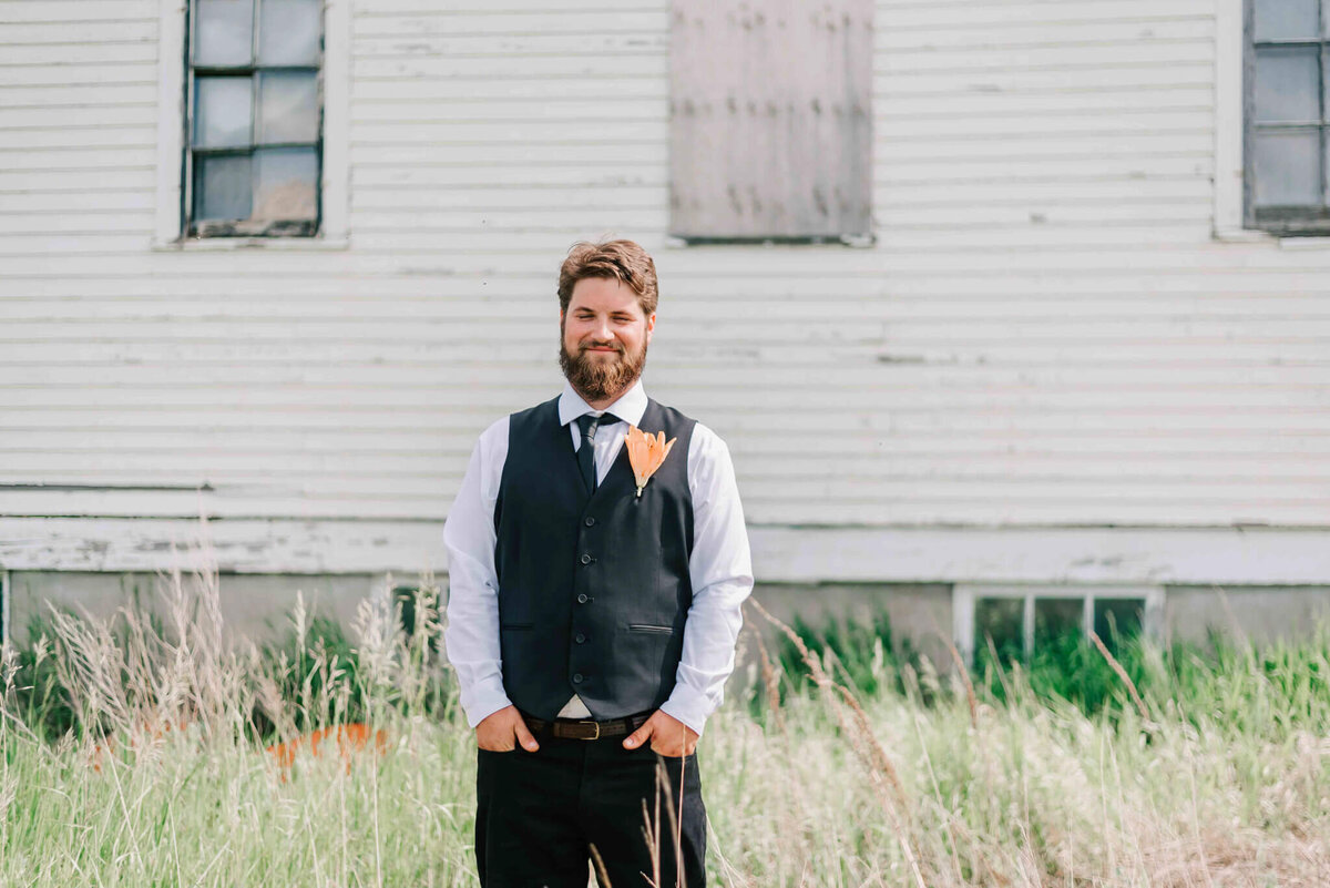 Groom standing by himself with hands in pockets in front of an abandoned church.