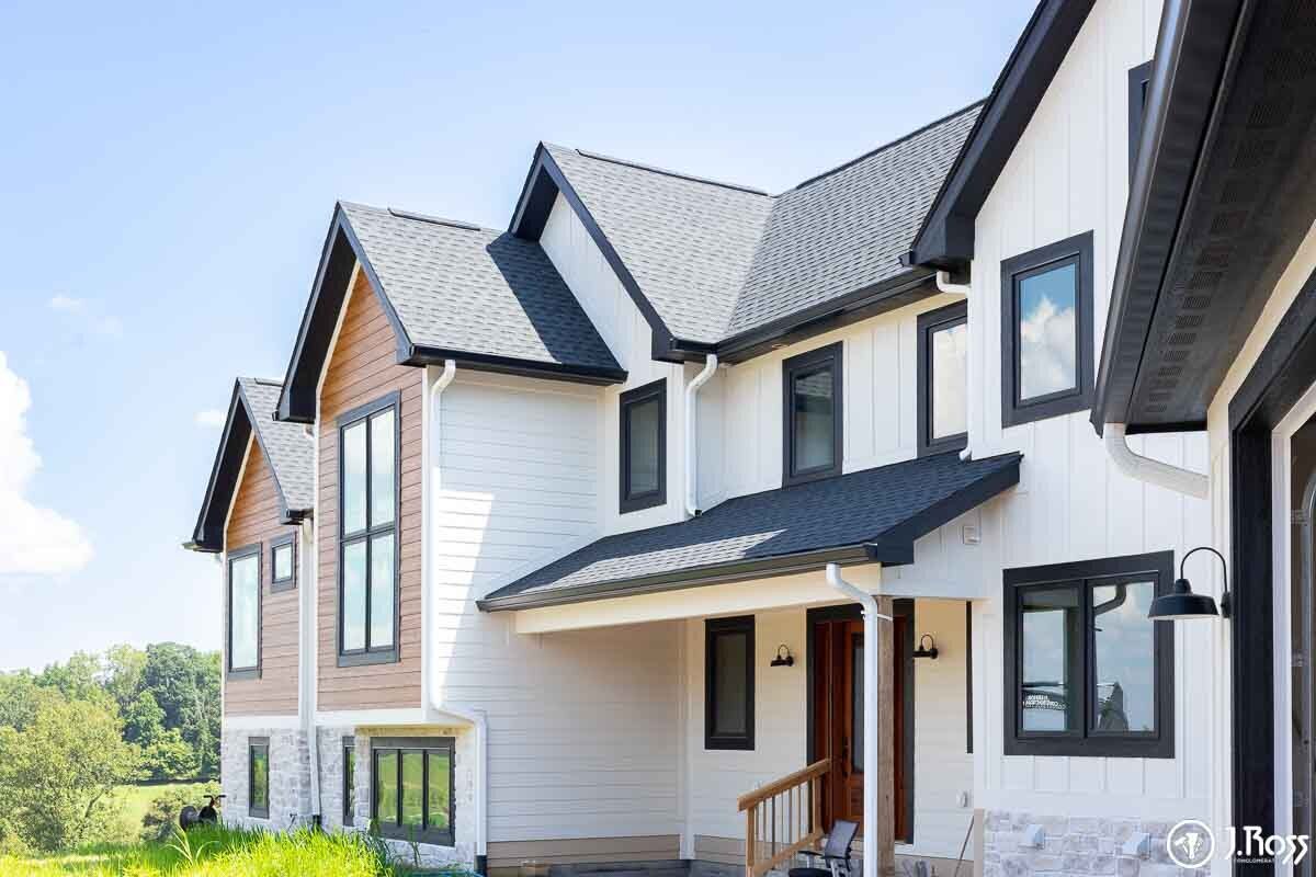 Close-up of the front entrance area, showing the porch roof, natural wood door and railings, white siding, and black gutters; examples of custom home outside painting, Kingsport, Tennessee.
