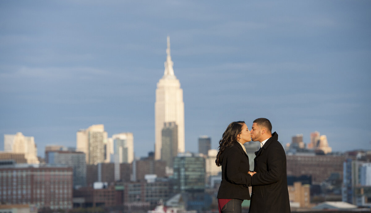A couple kissing with a city skyline behind them 