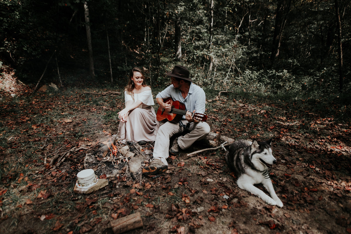 Couple sitting around a fire with their dog and cake