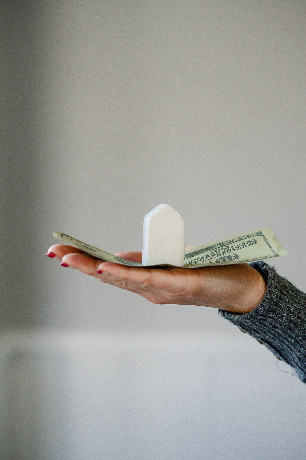 product photography near me with a hand holding a 100 dollar bill with a little white house on top of the money