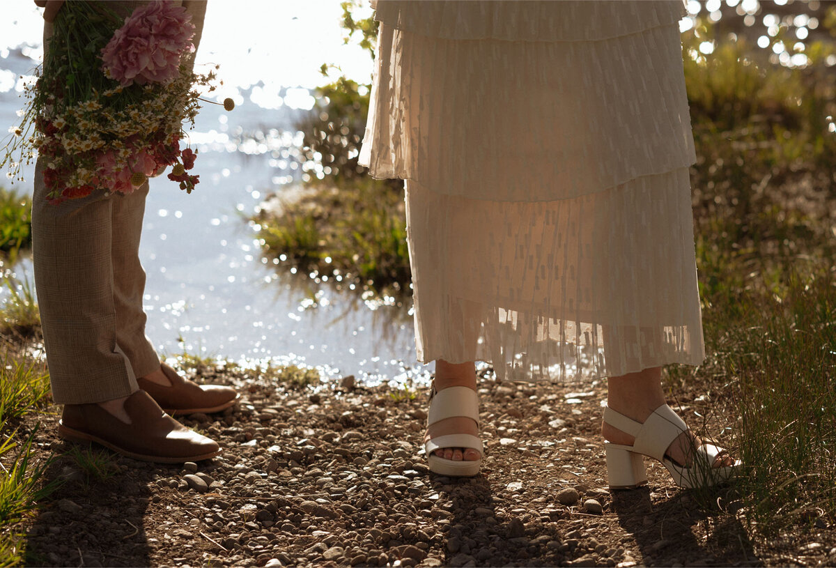 close up of bride's white dress and wedding shoes as she stands near Sparks Lake in Bend, OR