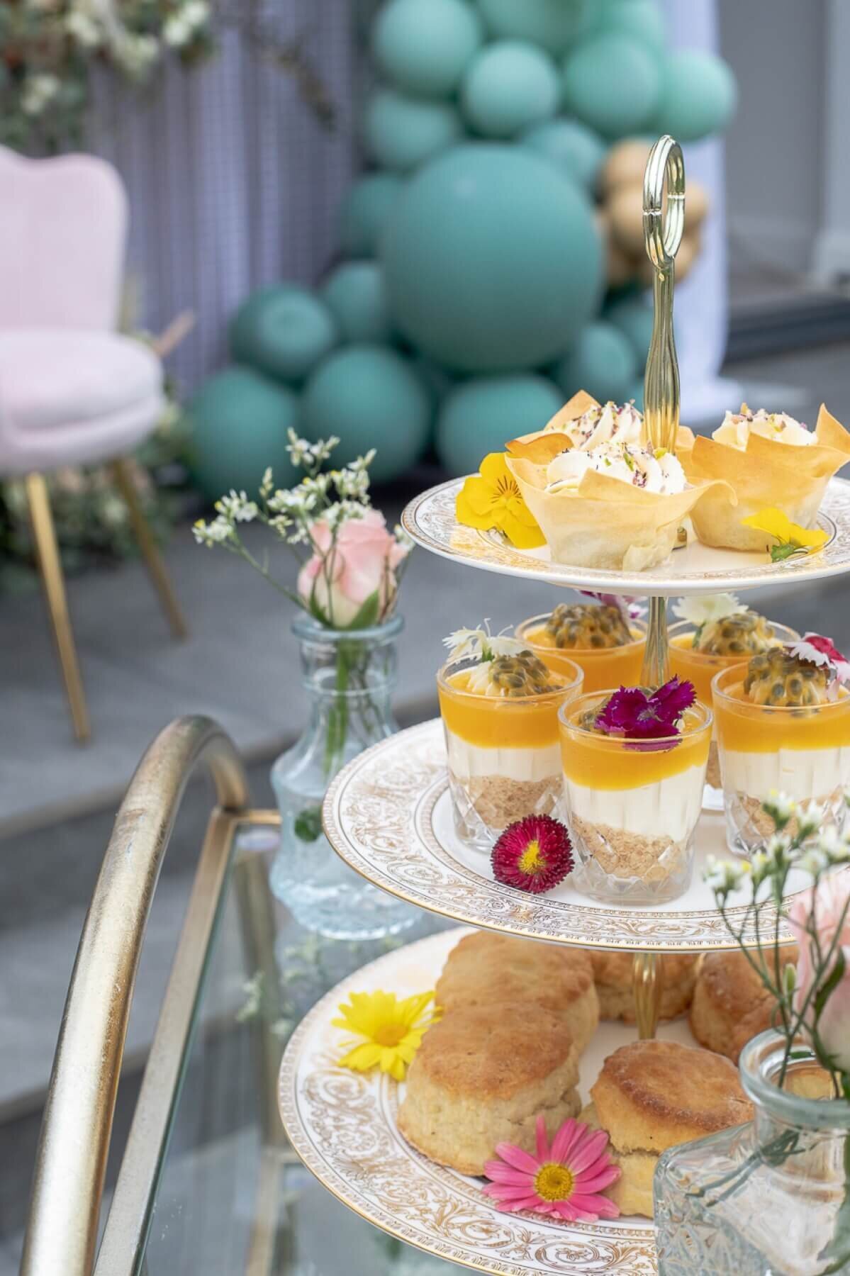 Afternoon Tea cake stand with mini desserts and scones with small flowers in glass jars