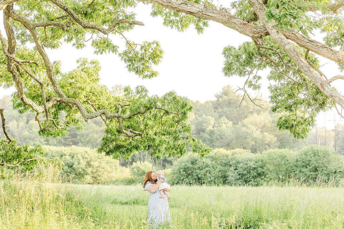 mom holds baby in field at charles river peninsula during family photo session  with sara sniderman photography