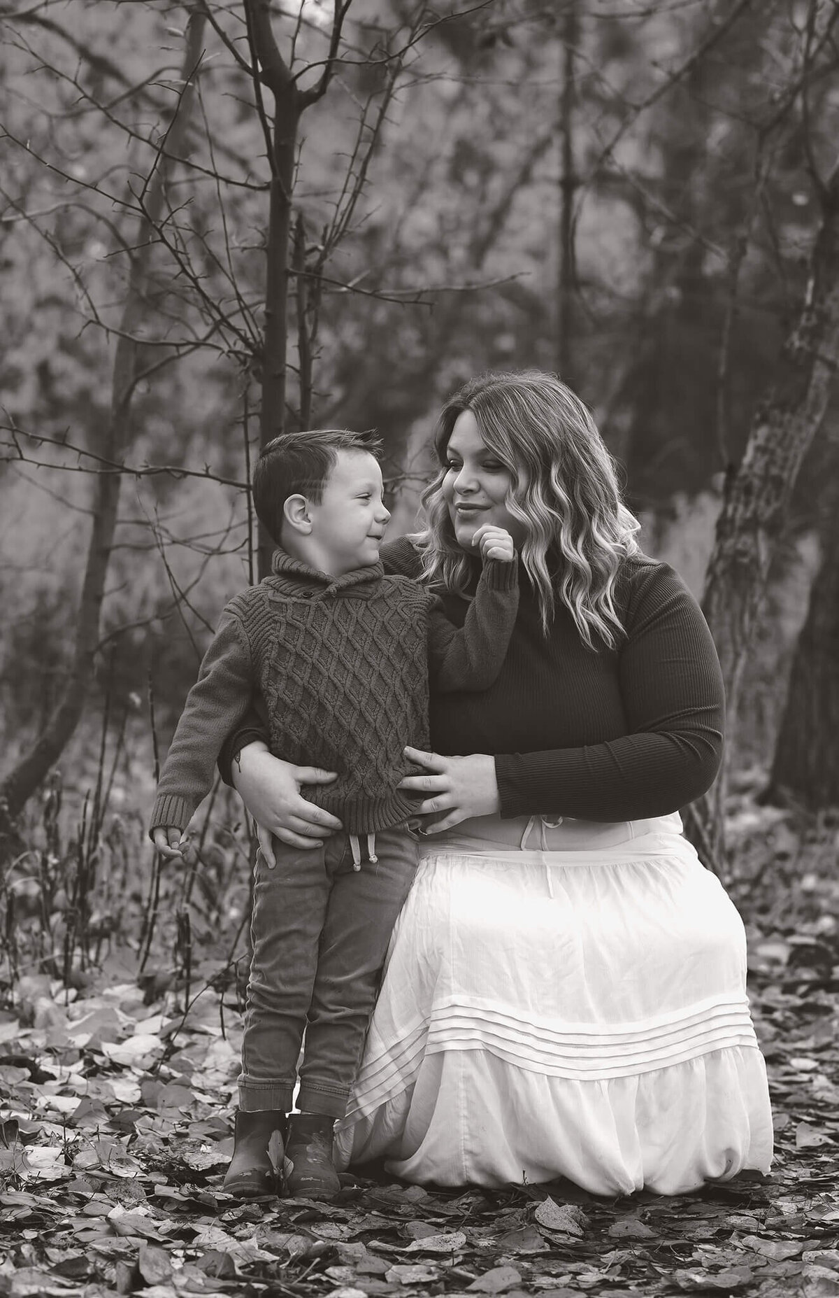 A black and white motherhood portrait taken by Brittany Danielle in Kamloops. A mom is crouched down to her sons level and hugs him from the side. He looks at her lovingly and grazes her cheek.