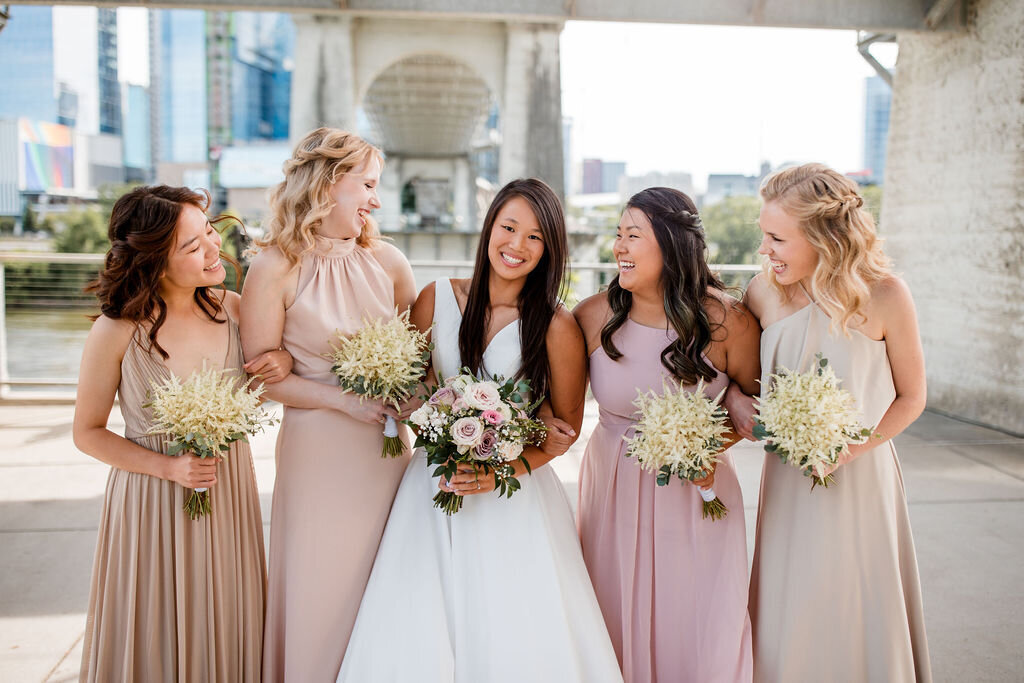 Bride and bridesmaid smiling under nashville bridge carrying bouquets in white and blush flowers