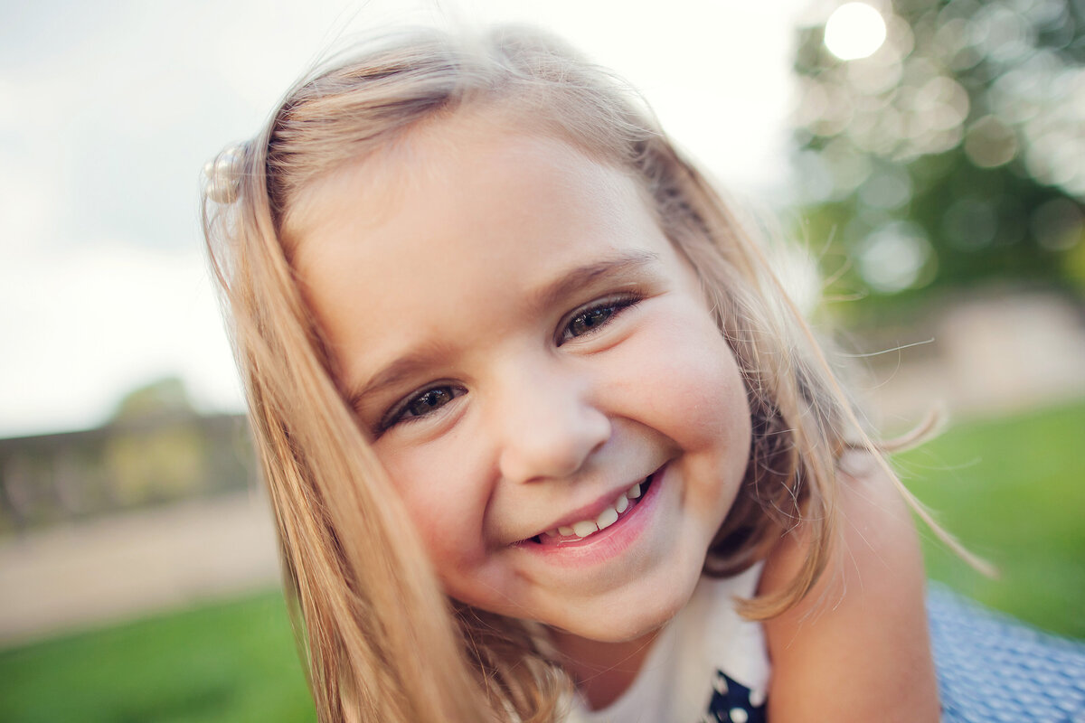 Close-up photo of a little girl giggling while she tries to get really close to the lens.