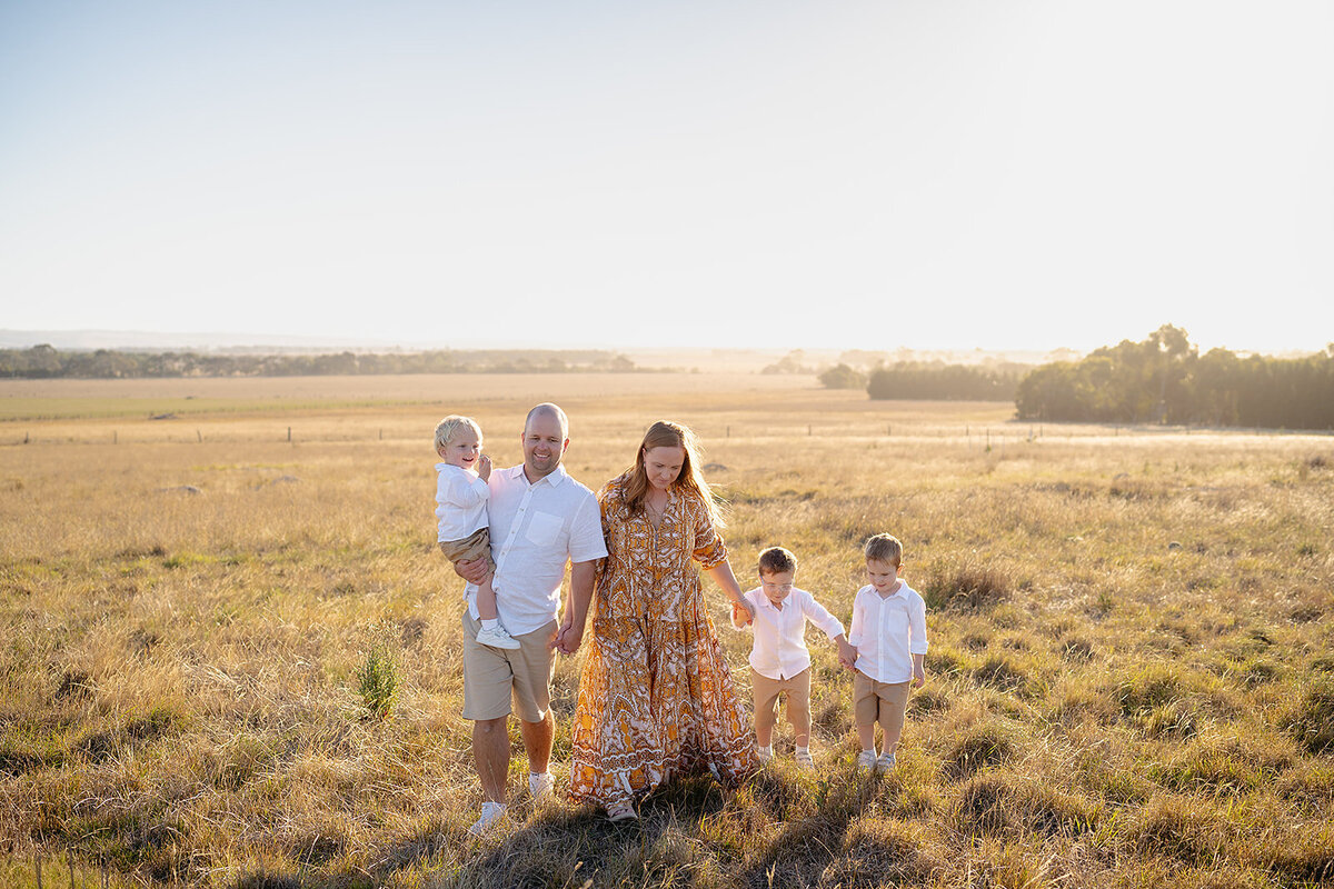 Golden hour family photography in rural Geelong, capturing parents with their three young boys walking through an open field in warm, natural light.