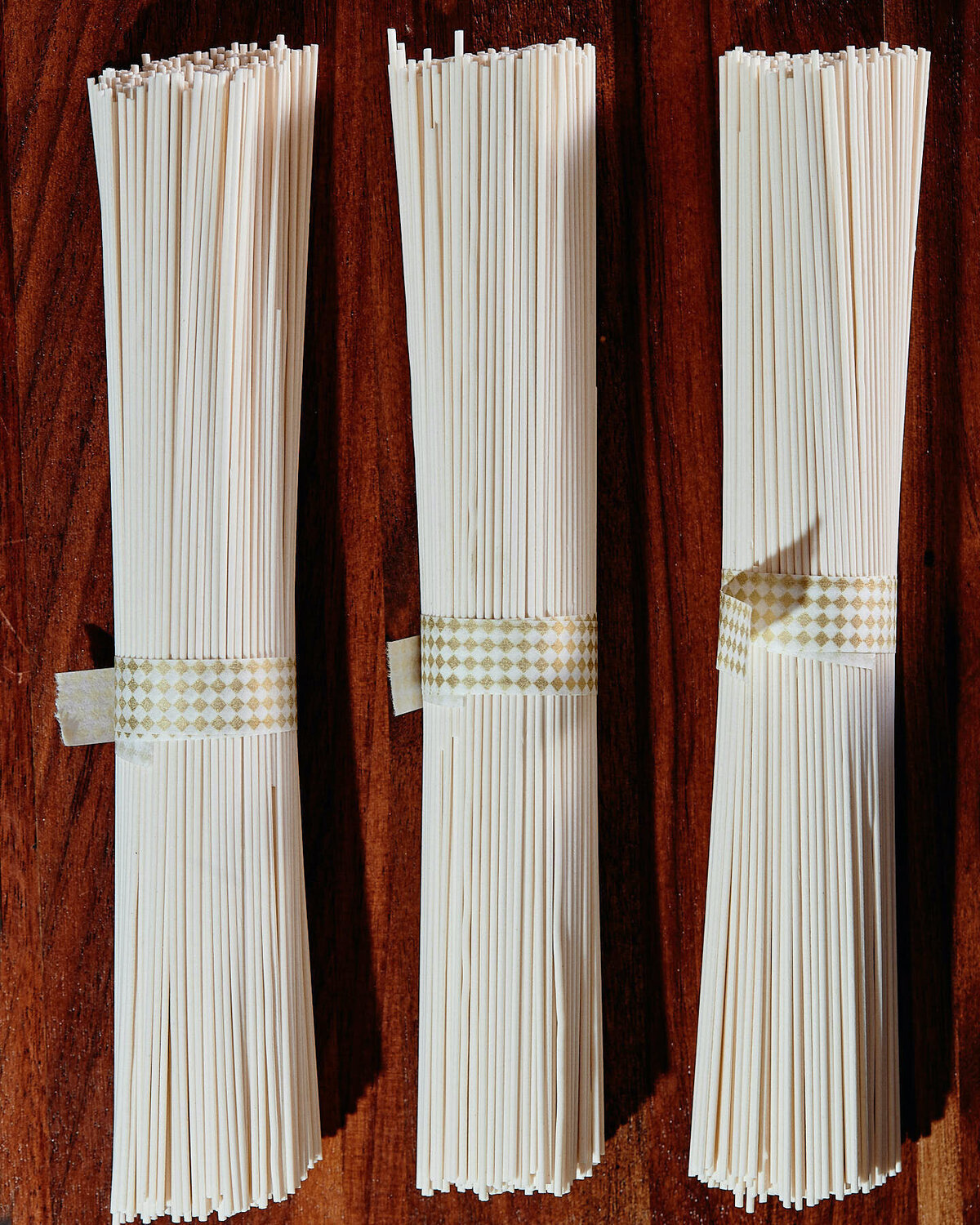 A minimalist image featuring neatly bundled dry noodles arranged on a wooden board. Captured by Mica McCook, this photograph showcases the simplicity and texture of traditional ingredients in a clean, elegant presentation.