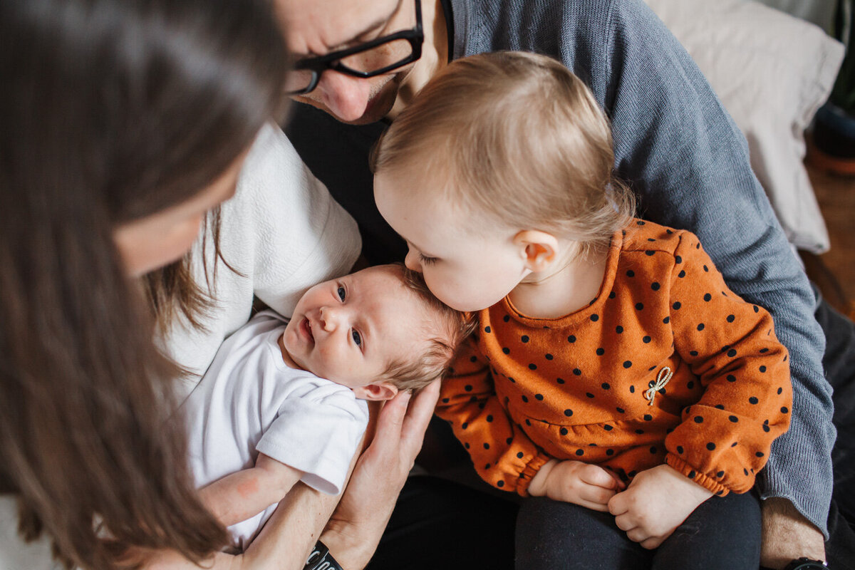 close up of big sister giving newborn sister kiss on head