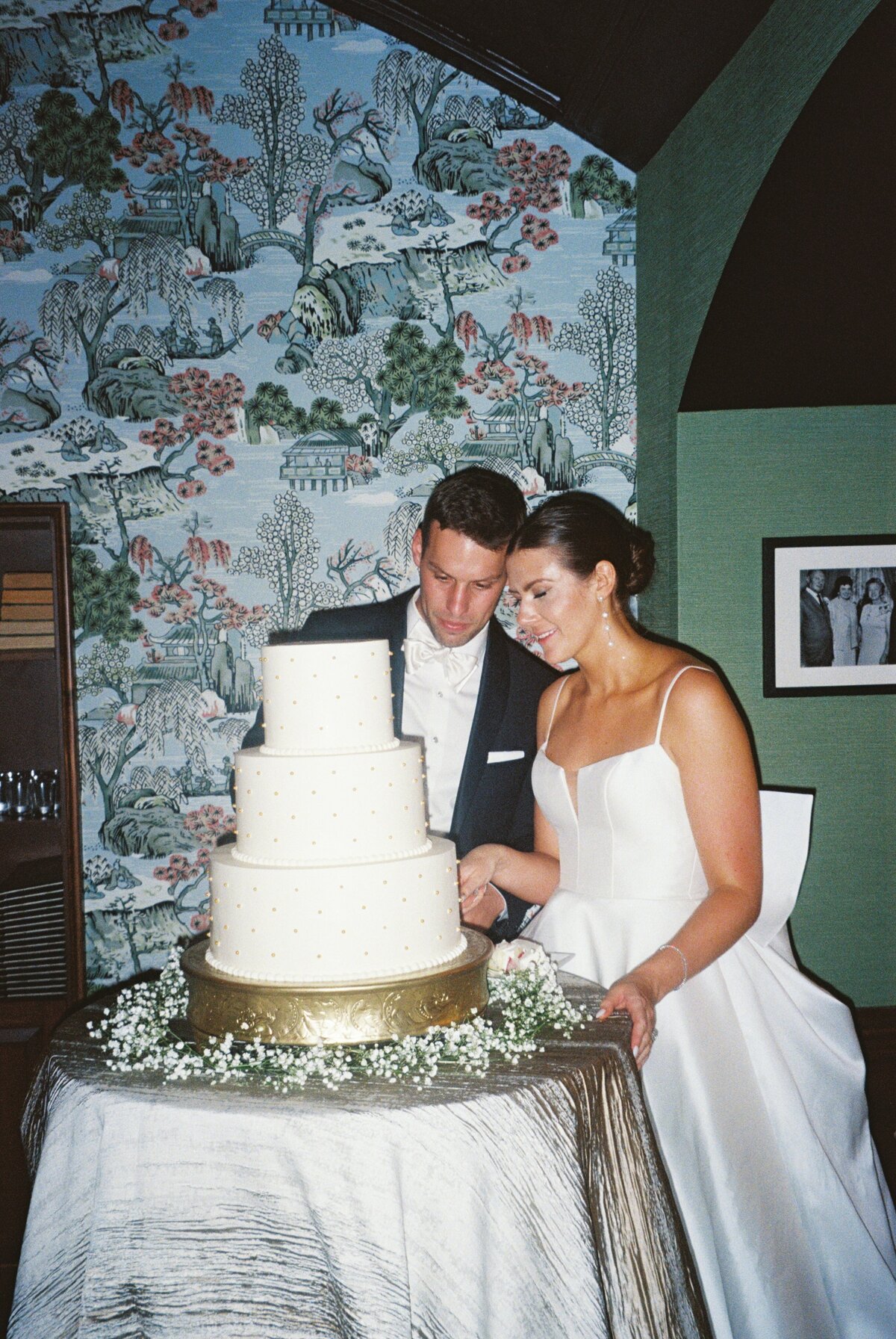 The bride and groom cut their wedding cake at The Madison Club, surrounded by funky wallpaper, captured on film to highlight this fun and memorable moment.