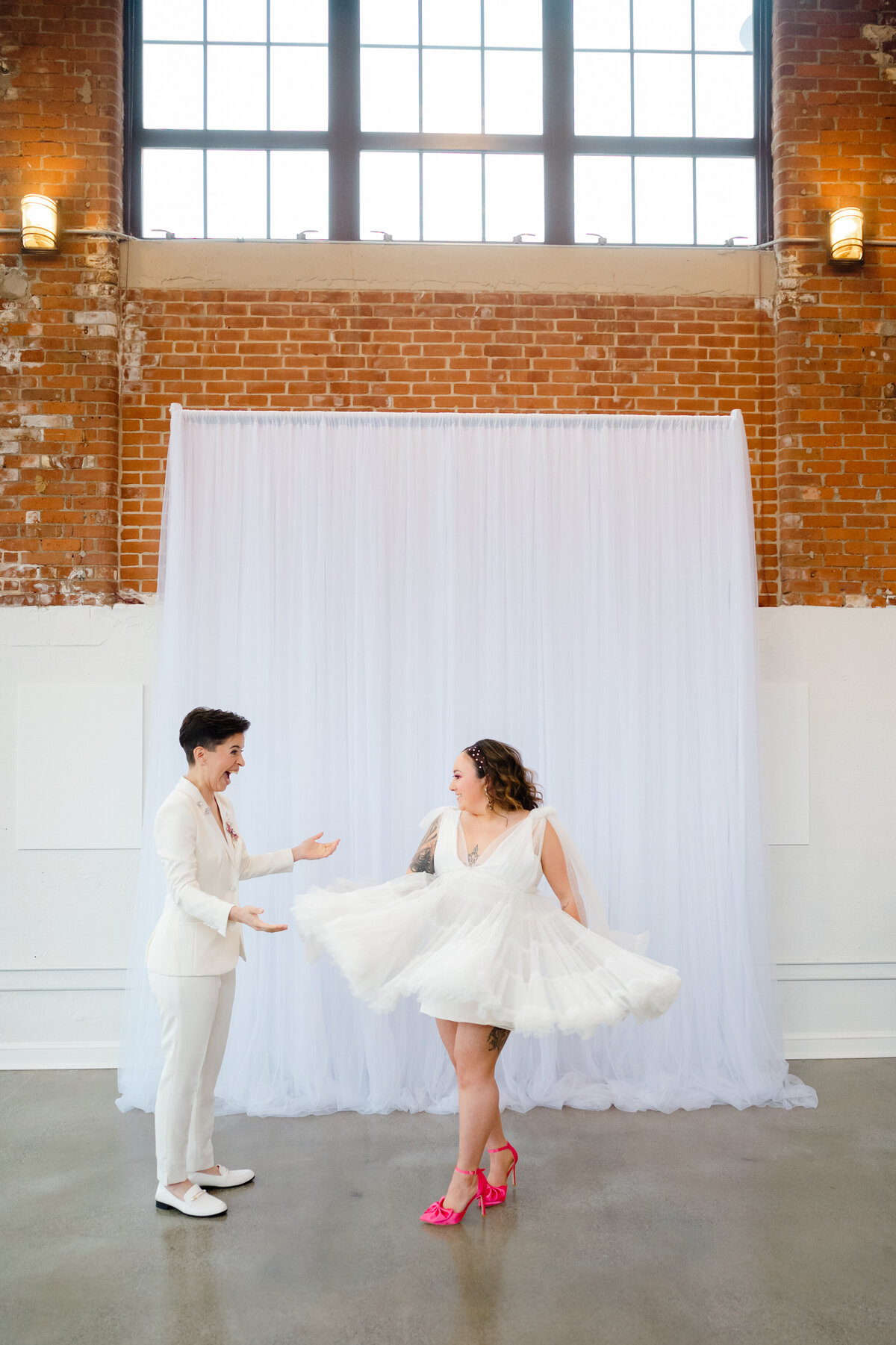 Bride twirling in her wedding dress while other bride watches