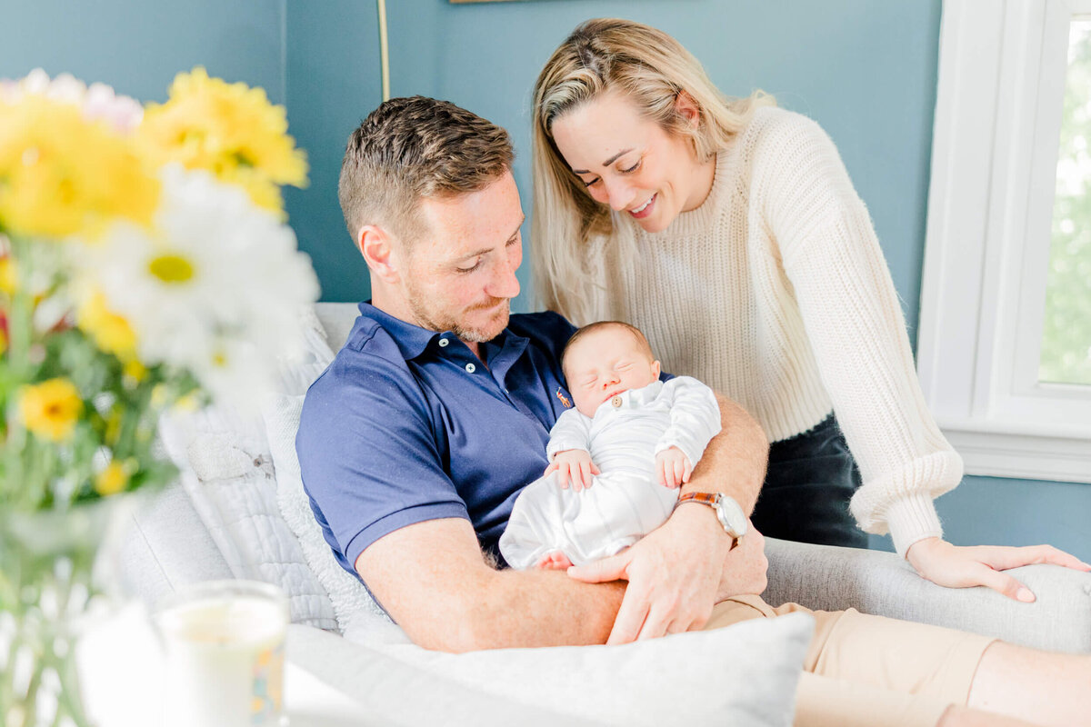 A mom and dad look at their newborn in dad's arms