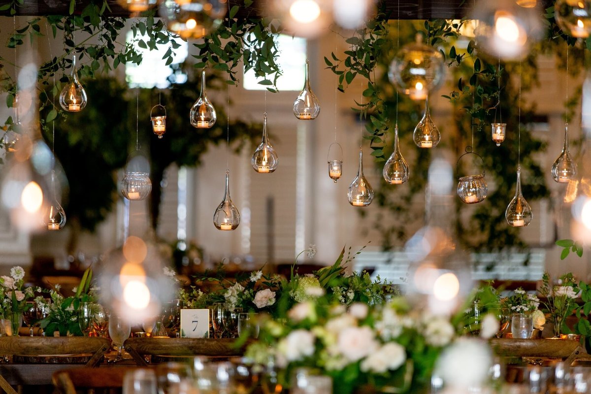 wooden trellis above dinner tables with greenery vines and hanging glass candles and glass orbs