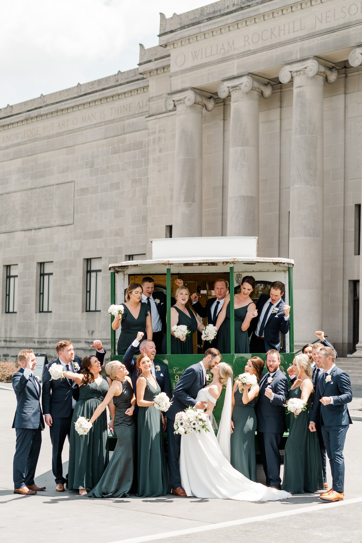 emerald and navy wedding party cheering wedding couple with green trolley in front of the Nelson-Atkins Museum