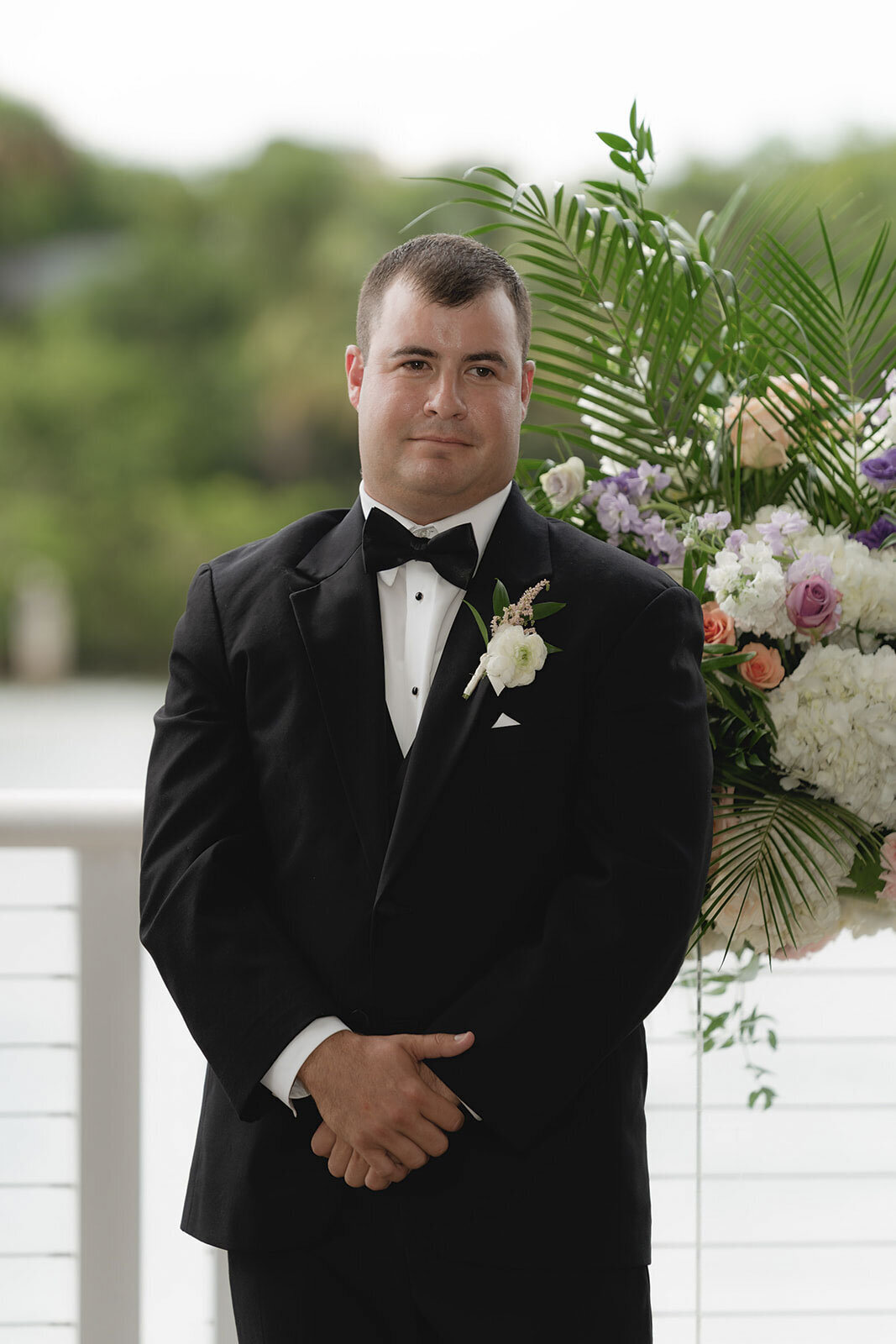 Groom standing next to floral bouquet at an outdoor wedding ceremony