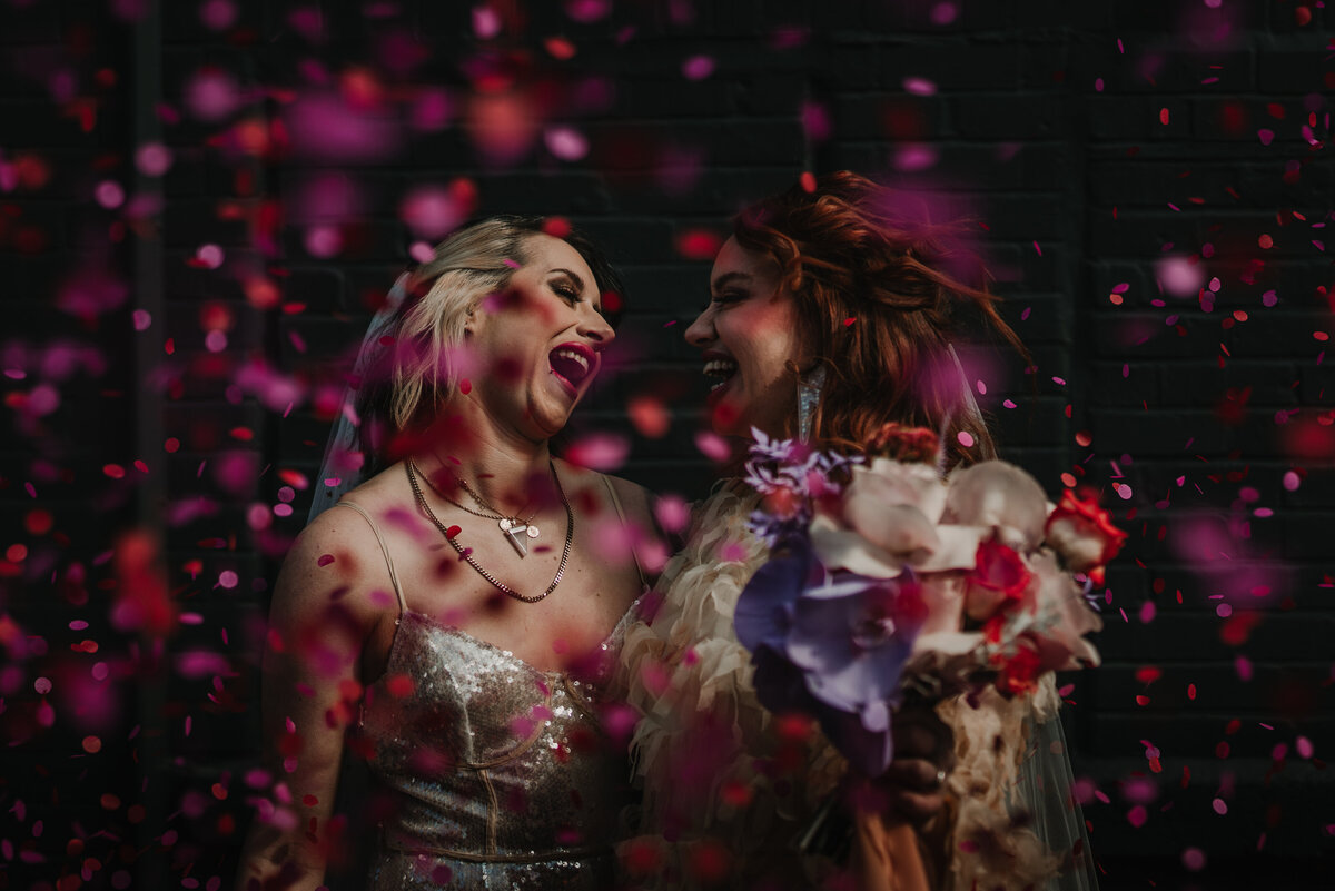 Alternative wedding photography of two brides in a blizzard of pink and purple confetti