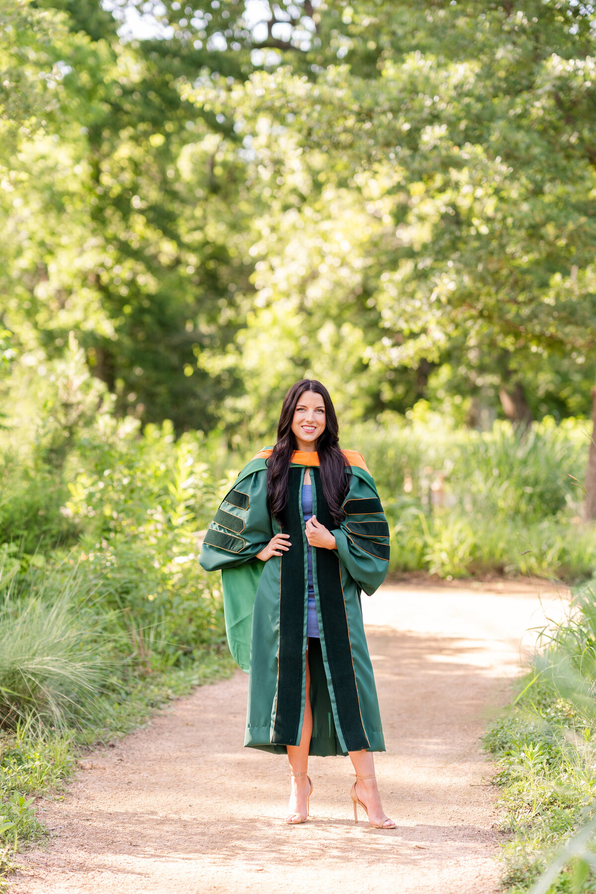 Baylor senior girl wearing doctorate gown and hood and smiling with hand on hip at the Houston Arboretum