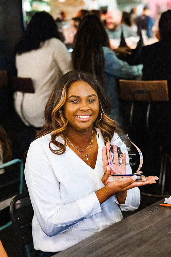 Woman in white jacket holds up award she just received at her company event.