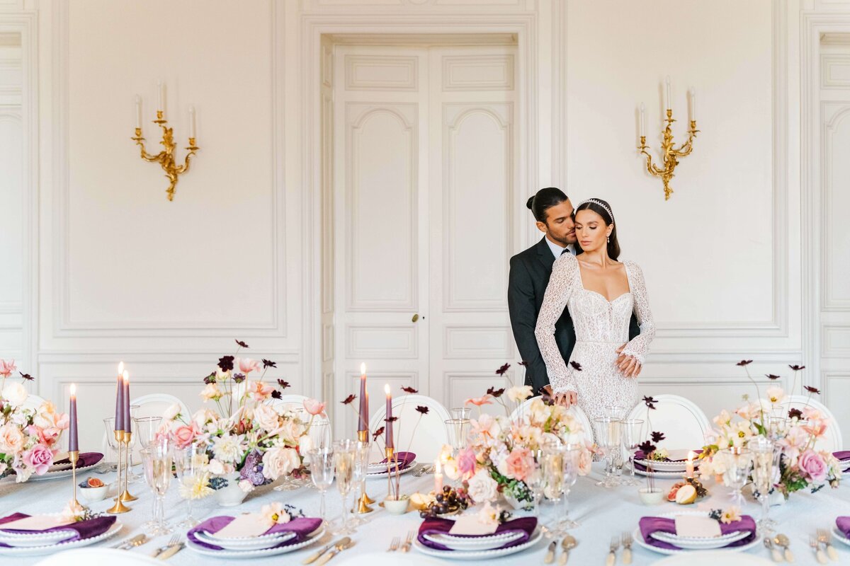 bride and groom standing behind a long table set up with flowers and plates