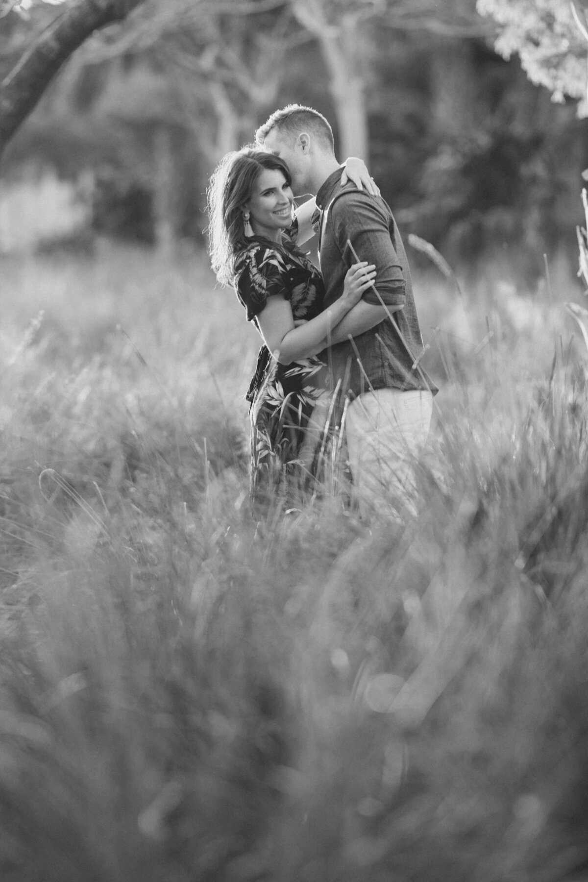 Black and white engagement portrait of a couple embracing in a grassy field, captured by Rodrigo Varela Photography in Miami, Florida. Rustic and romantic outdoor setting emphasizing natural beauty.
