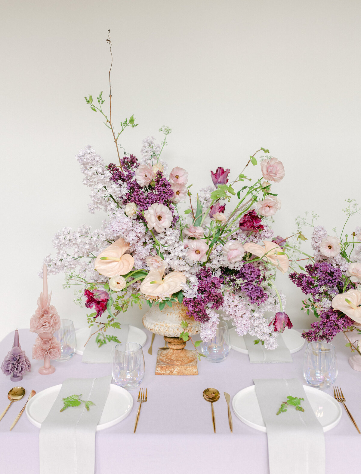 An arrangement of spring flowers featuring lilacs and colourful greenery sits on a table.