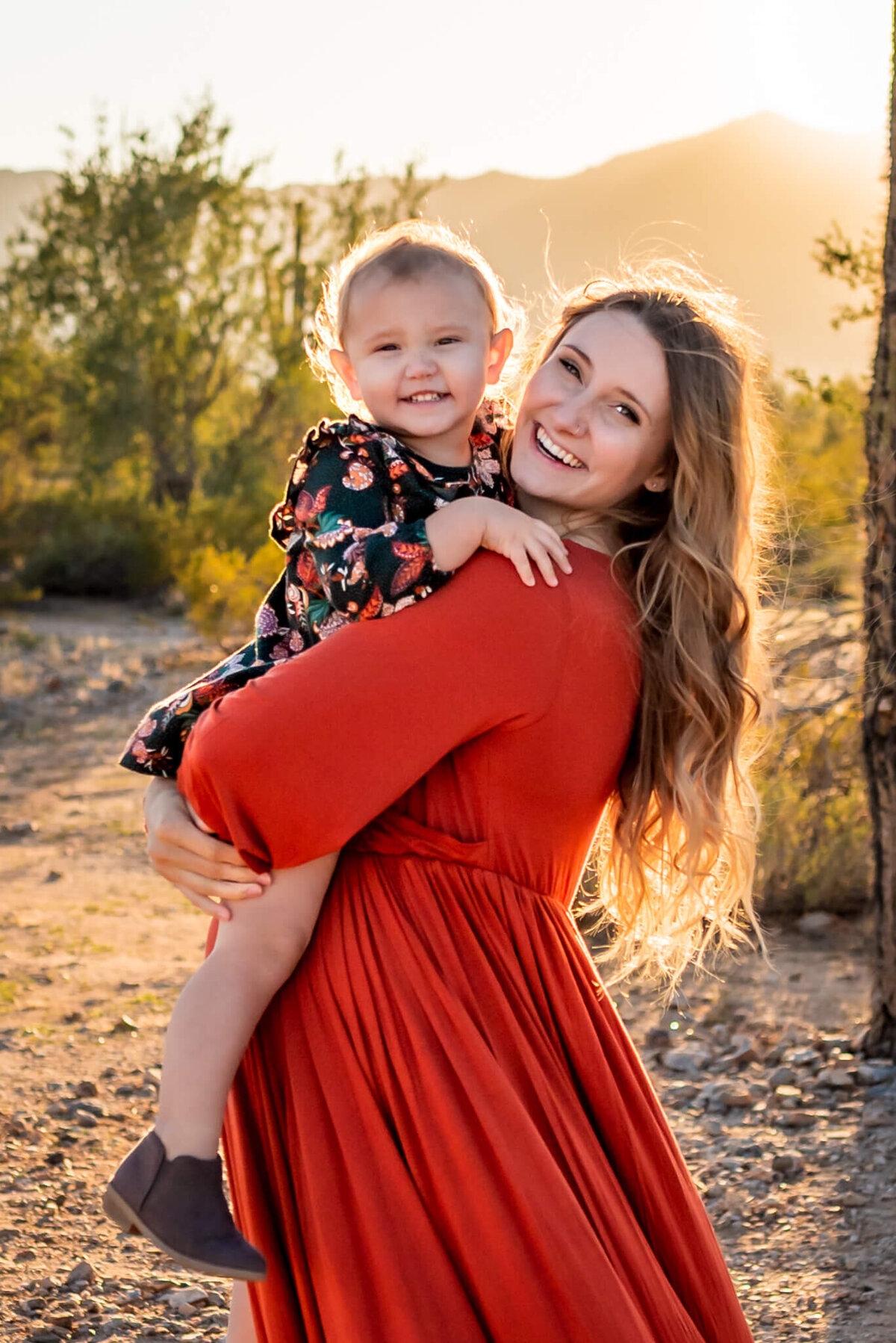 Mom to be hugging young daughter at sunset. Captured by Cactus & Pine Photography