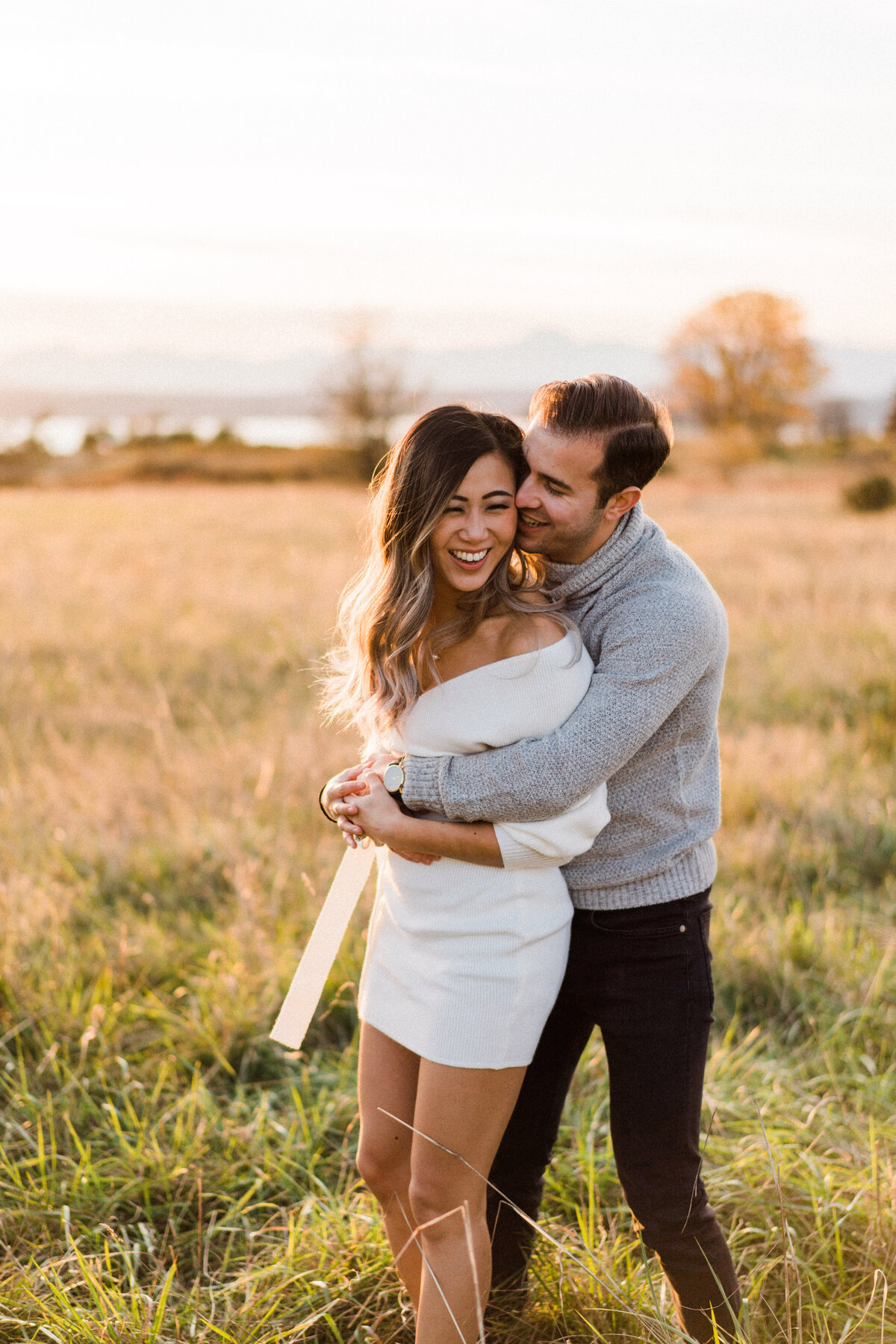 Couple kissing and embracing in large meadow at the best spot for engagement photos in Seattle, Discovery Park, in Magnolia