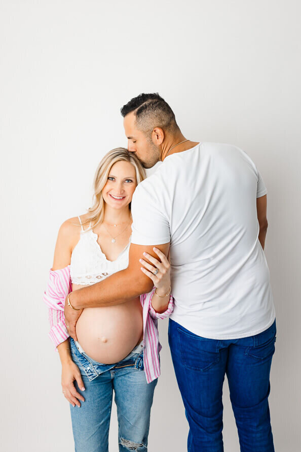 A man stand backwards, embracing his wife's pregnant belly as a part of their maternity photos.