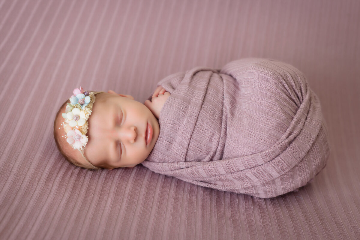 Newborn Photographer, a baby girl lays on the bed and wrapped in matching blankets