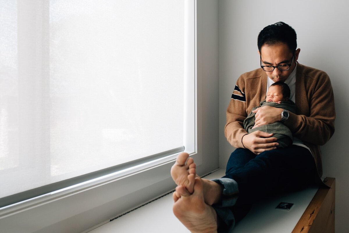 Dad holding baby as sits in window seat, Melbourne Newborn Photography and Lifestyle Family Photography