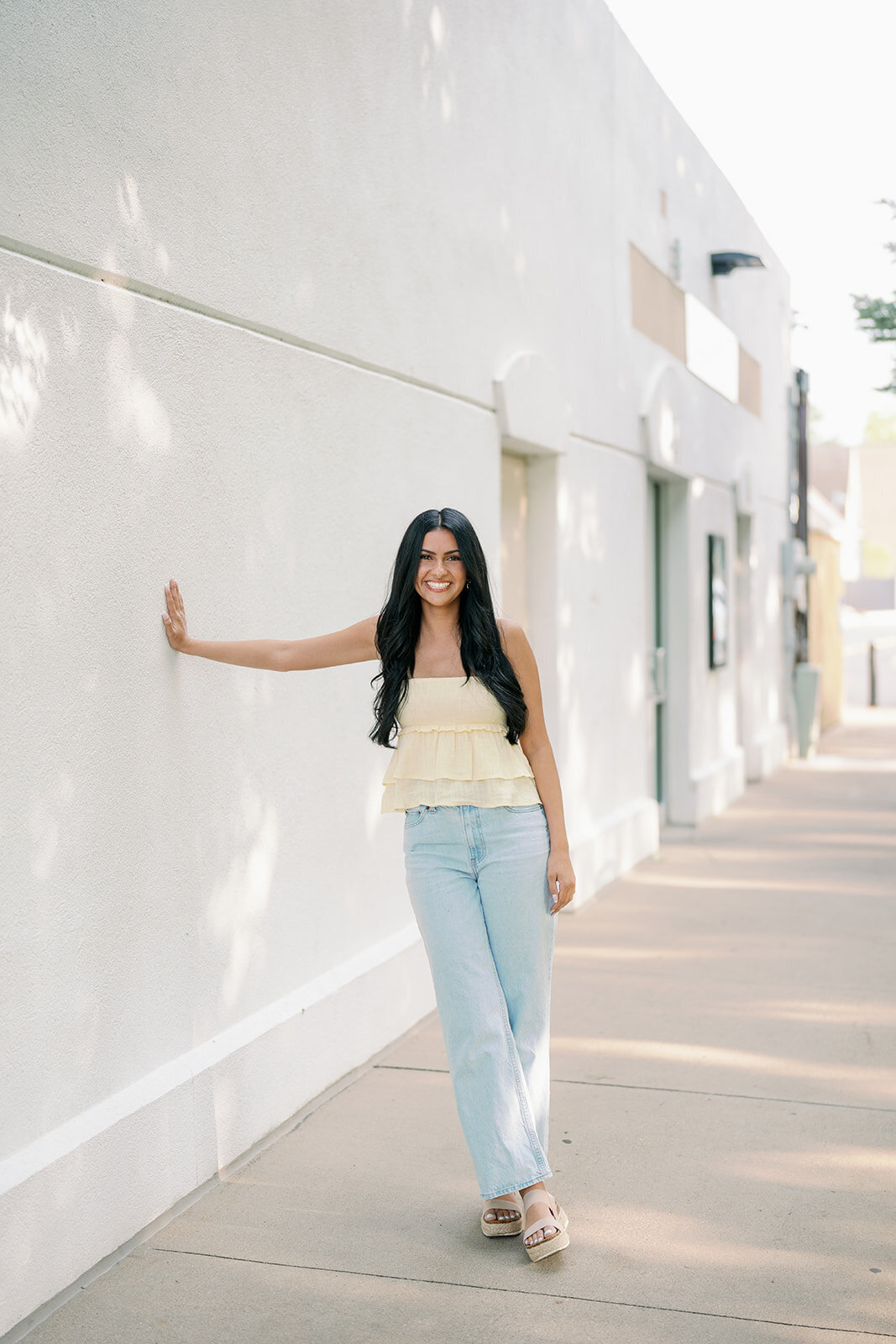 High school senior posing against a white wall in downtown South Haven during her Michigan senior photo session.