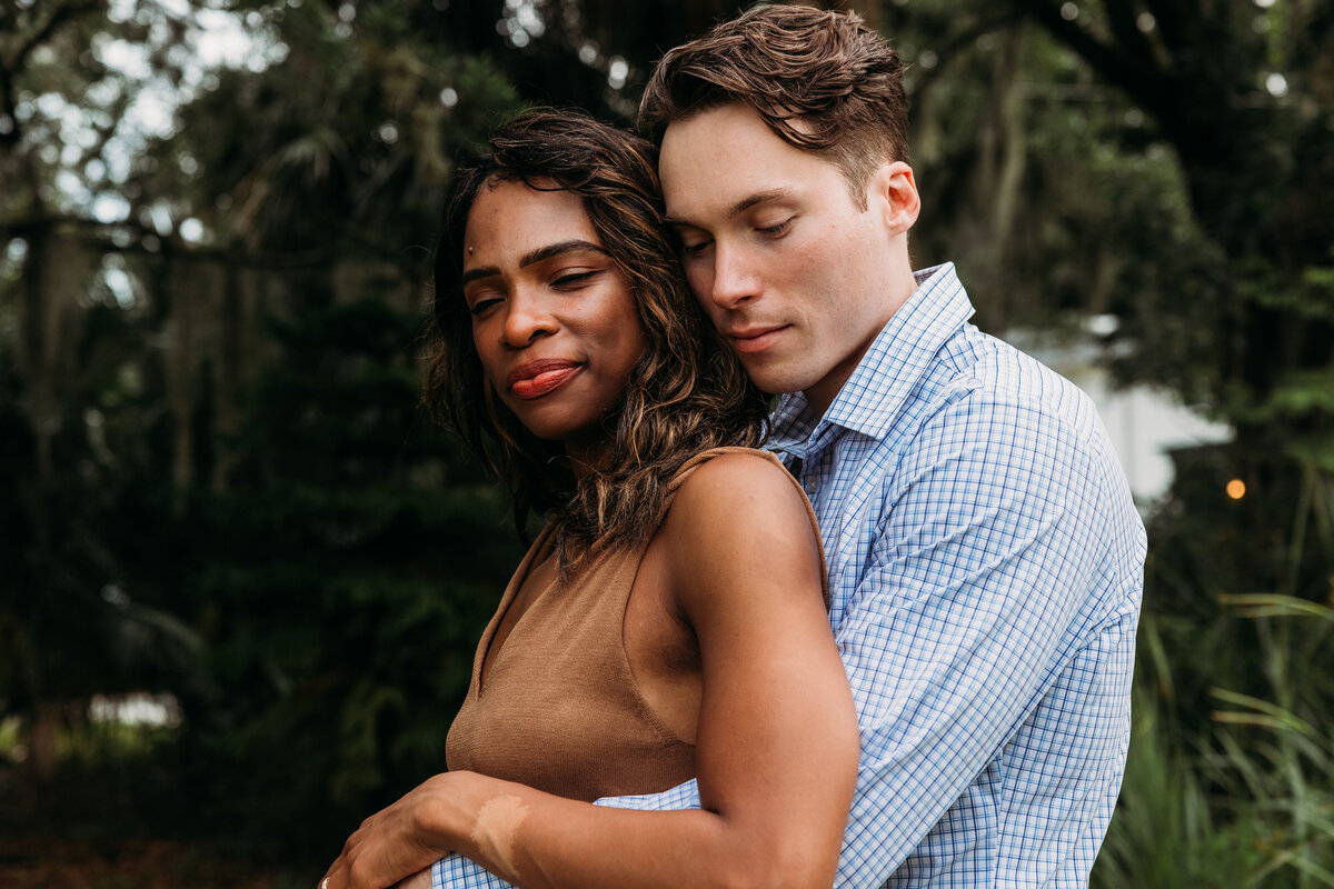 Couple stands peacefully embraced, eyes closed, under soft Florida light in a mossy oak garden during their Jacksonville engagement session