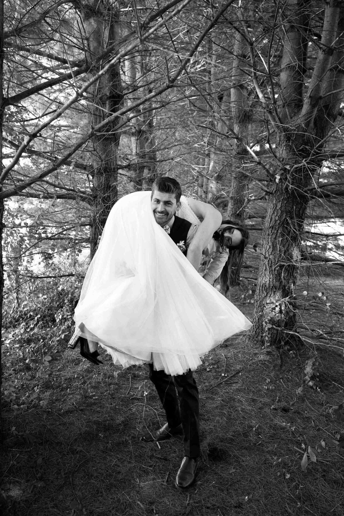 groom, playfully picking up his bride and carrying her through the woods on a farm in Pennsylvania