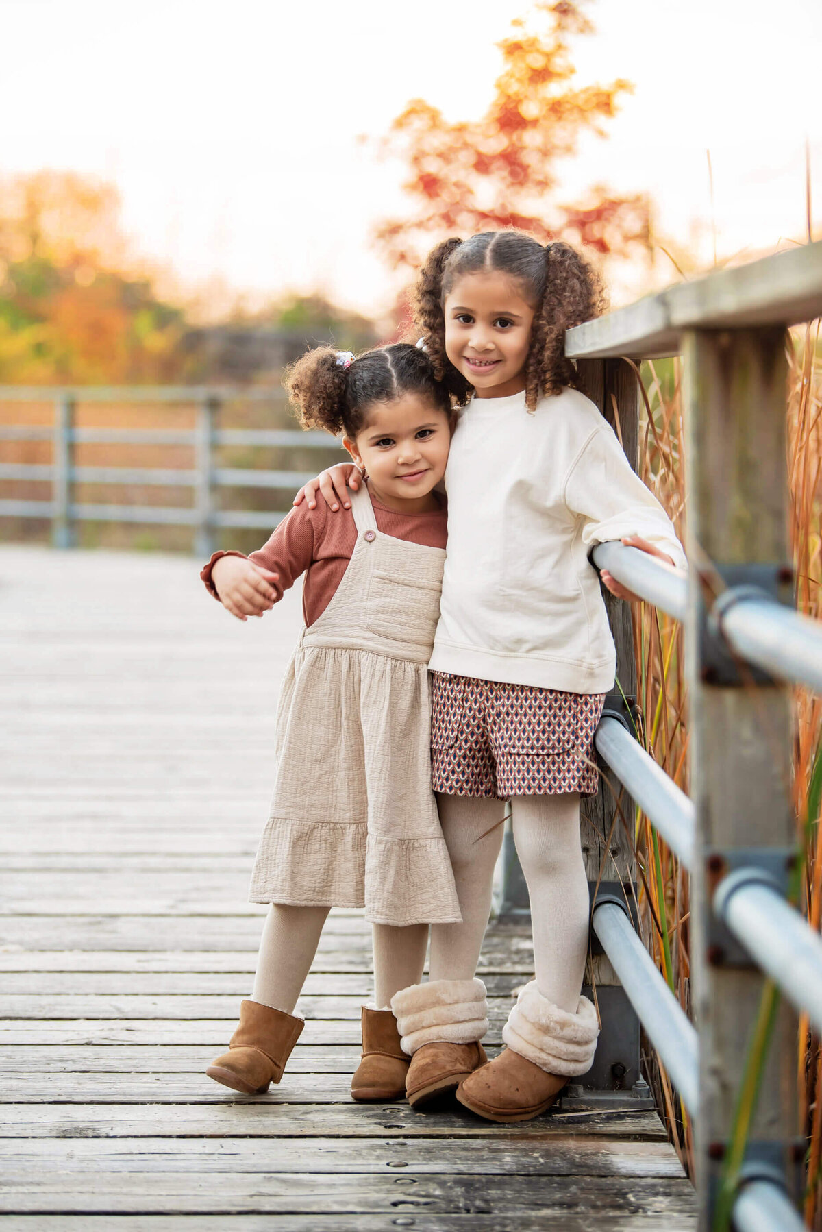 sisters standing on a bridge with the golden sunlight behind them for their Burlington, On family photos