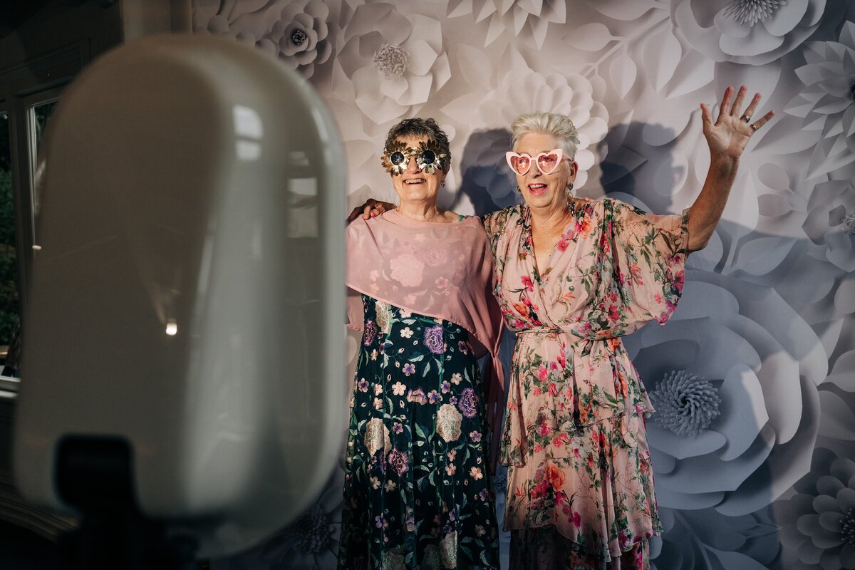 two women behind the screen of a white modern freestanding photo booth at a wedding