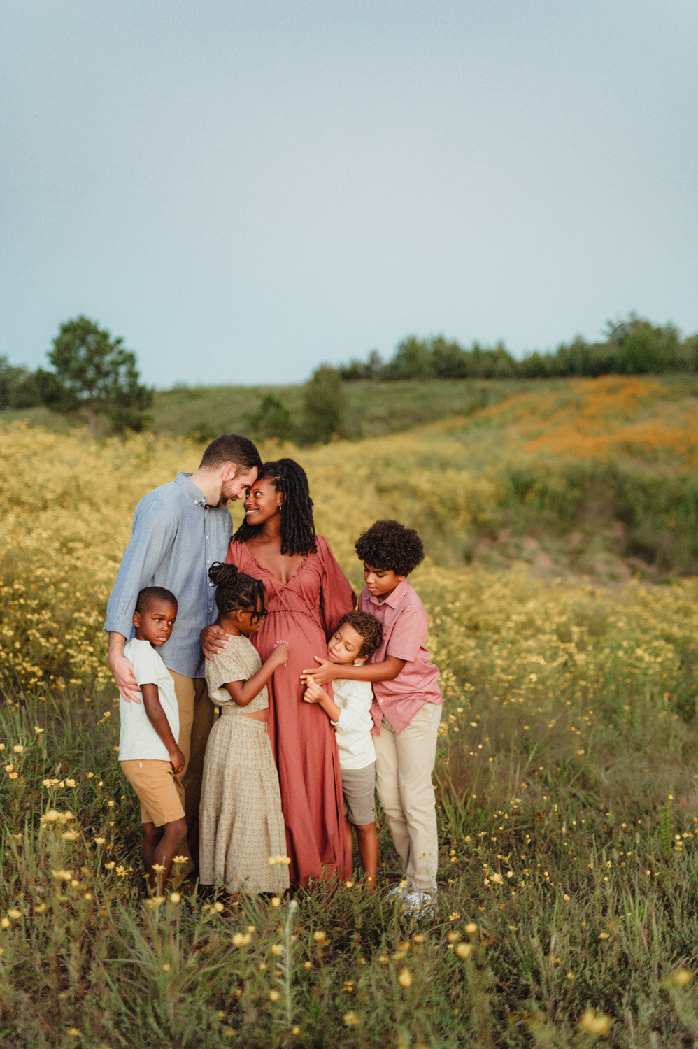 Expecting mother embraced by her children and partner in a field of flowers during Greensboro maternity photoshoot