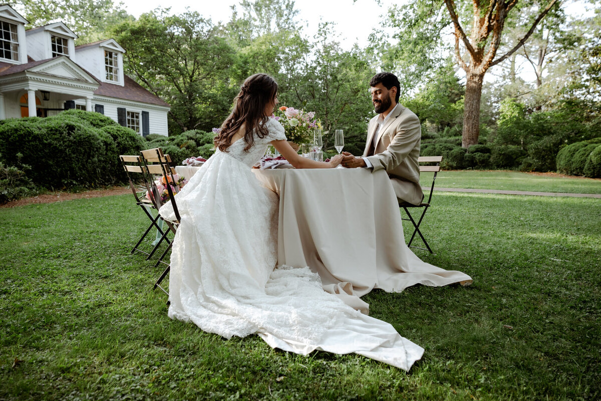 Bride and groom sharing a quiet moment at a table set up in a garden, surrounded by spring greenery.
