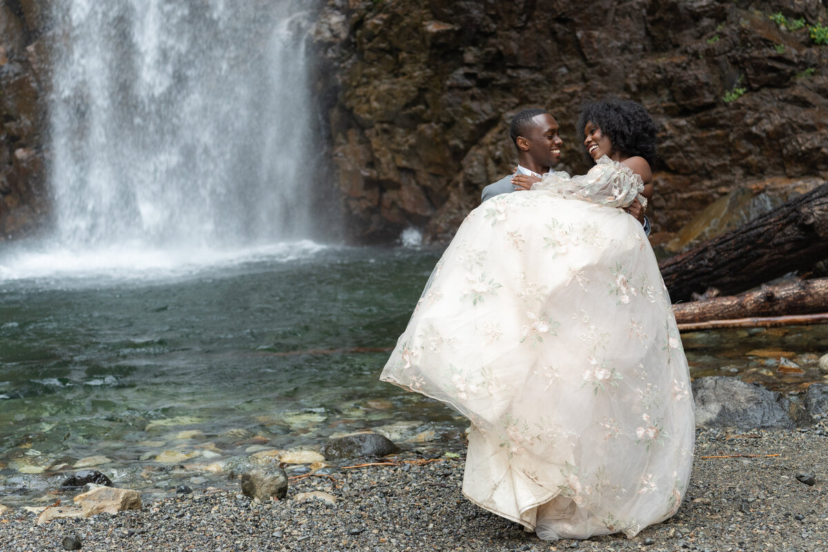 A person holding their partner up in front of a waterfall
