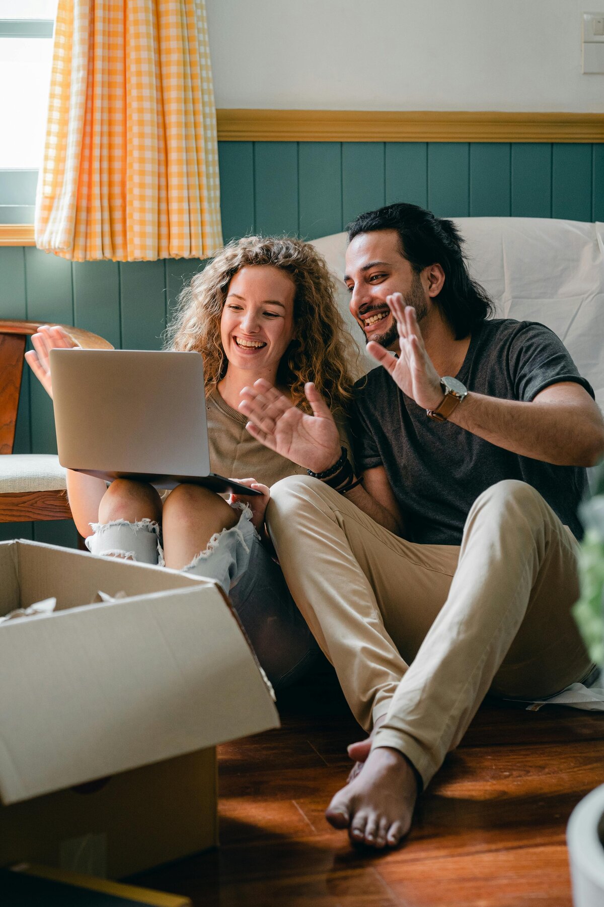 Man and woman sitting together looking at the computer waving and smiling