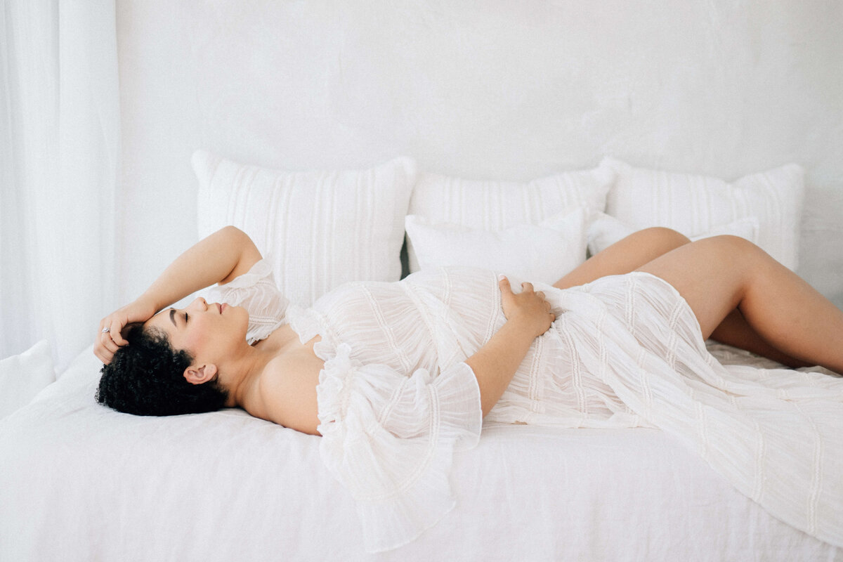 maternity mother laying on a bed with a hand across her belly