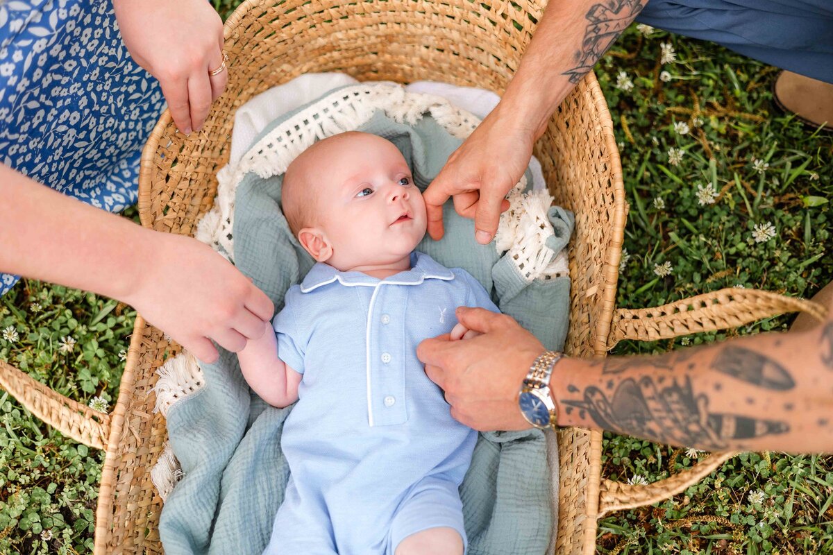 young family interacting with infant in a moses basket outdoors