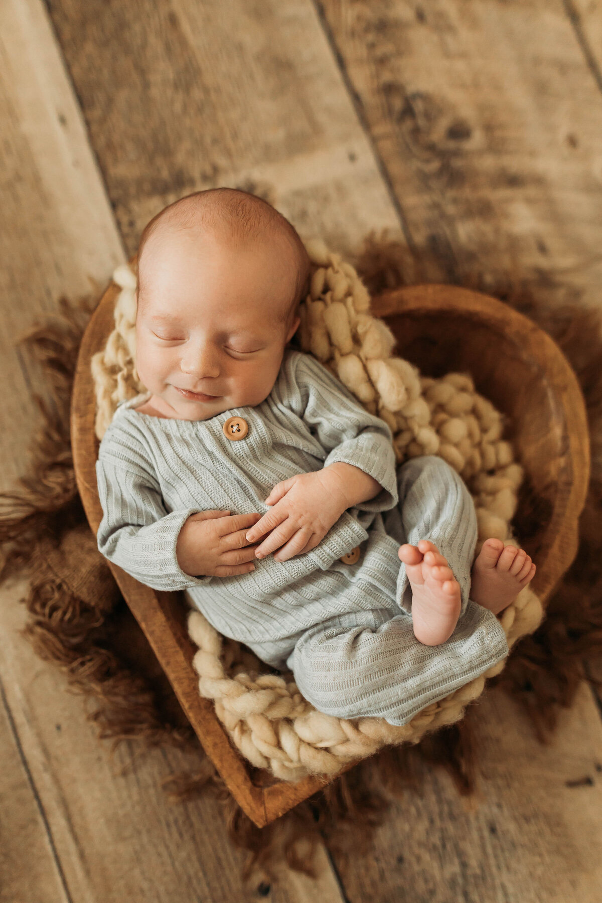 Small baby wearing a blue outfit laying in a heart shaped basket with a smile.