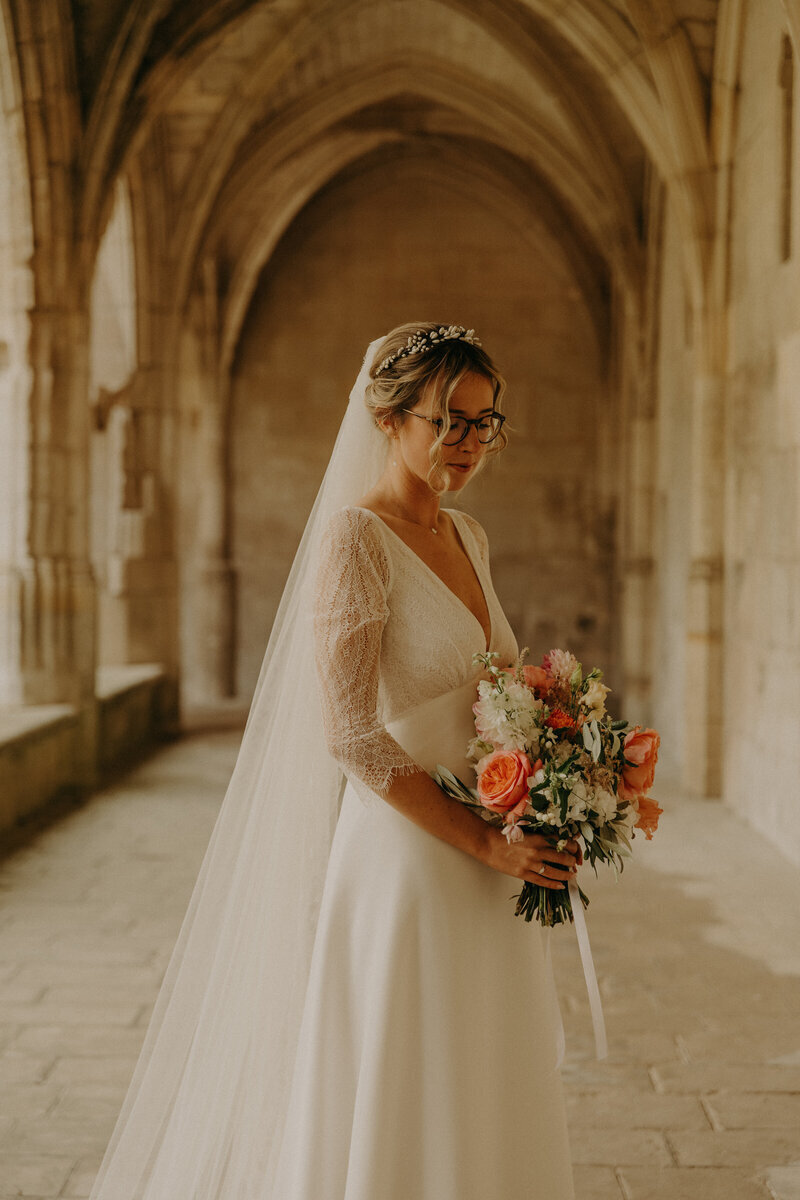 Mariée posant pour Laura, photographe professionnelle en Vendée, sous des voûtes en pierre avec son bouquet.