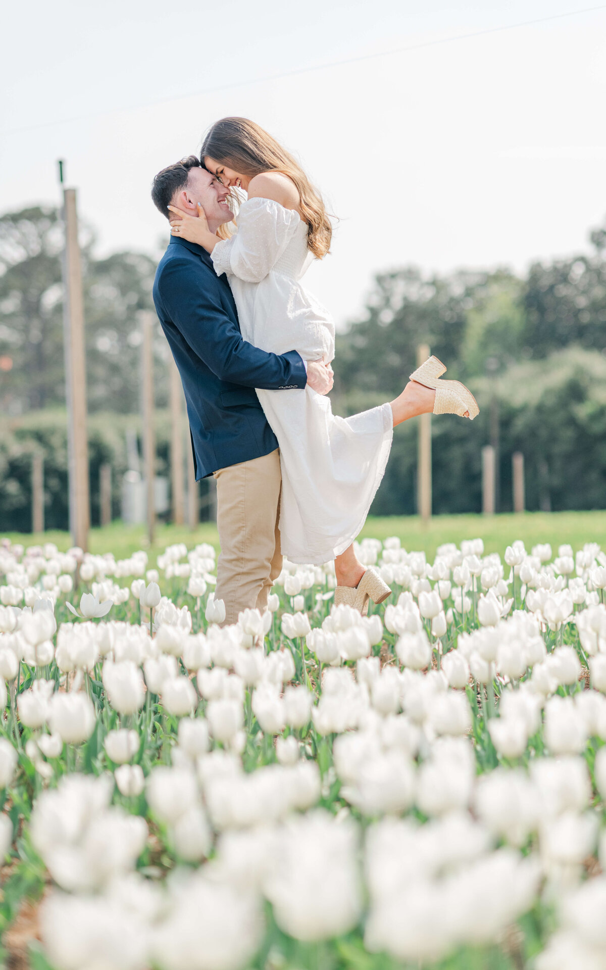 Man holding womnan up and kissing in a field of white tulips for engagement photos